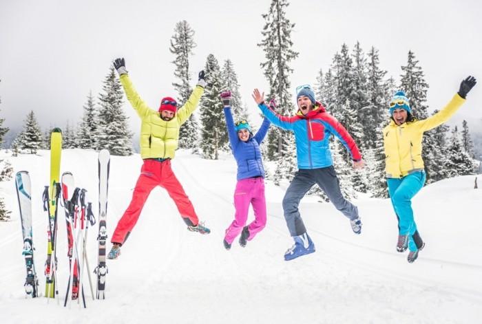 Eine vierköpfige Familie springt auf einer Skipiste vor Freude in die Höhe winterurlaub